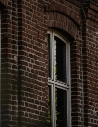 TRYBA_Belgique_fenetre_1.webp Une fenêtre encadrée de briques rouges, laissant entrevoir des reflets sur le verre.