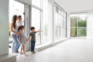 tryba_belgique_fenetre.webp Une famille observe l'intérieur lumineux d'une maison moderne avec de grandes fenêtres.