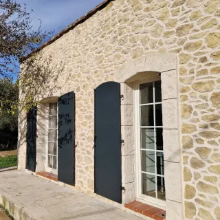 volet_battant_aluminium.webp Façade en pierre d'une maison traditionnelle avec des volets en bois sombre.