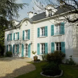 volets_battants_choix_responsable.webp Belle maison traditionnelle avec volets turquoise et façades blanches, entourée d'un jardin verdoyant.