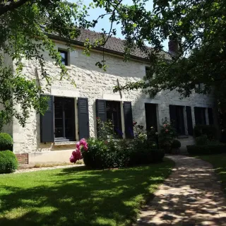 volets_battants_isolation_renforce.webp Charmante maison en pierres avec volets noirs et jardin fleuri sous un ciel bleu.
